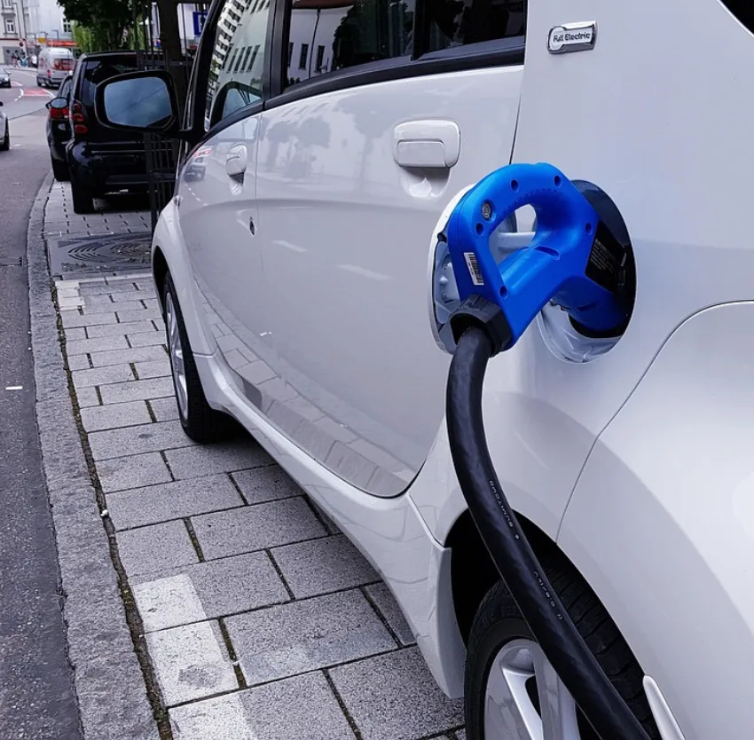 White electric vehicle plugged into blue charging point on urban street