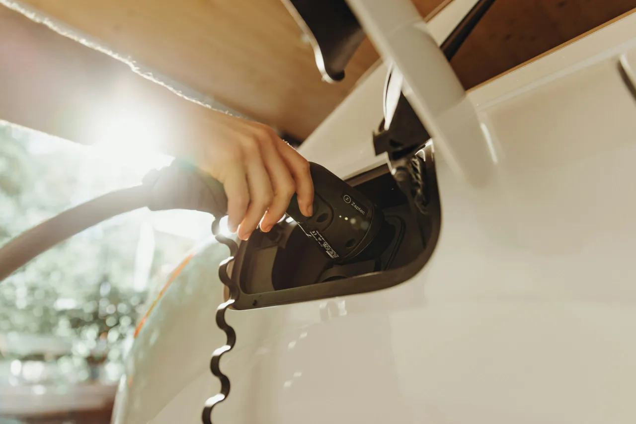 Hand inserting electric vehicle charging cable into white car's charging port