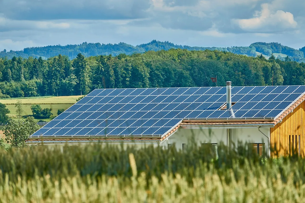 Modern building with solar panels on roof in rural landscape with fields and forested hills