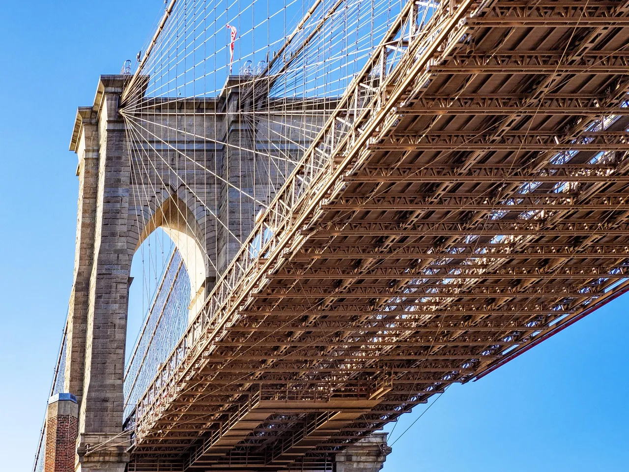 Historic suspension bridge with steel cables and ironwork against a clear blue sky
