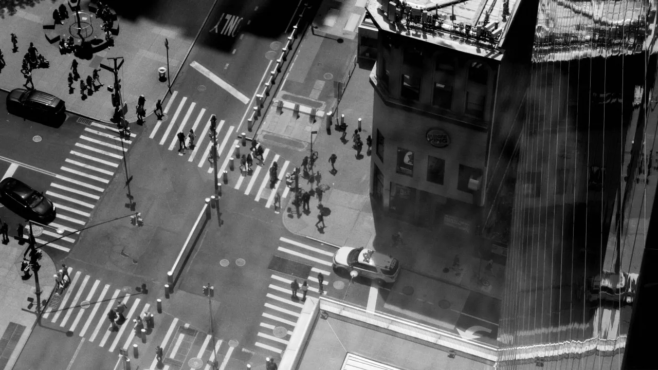 Aerial black and white view of a busy urban intersection with pedestrians crossing zebra crossings and vehicles
