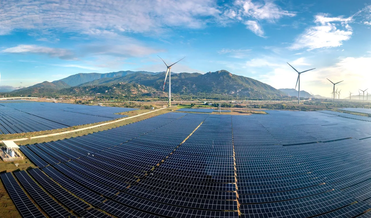 A solar farm and wind turbines below mountains