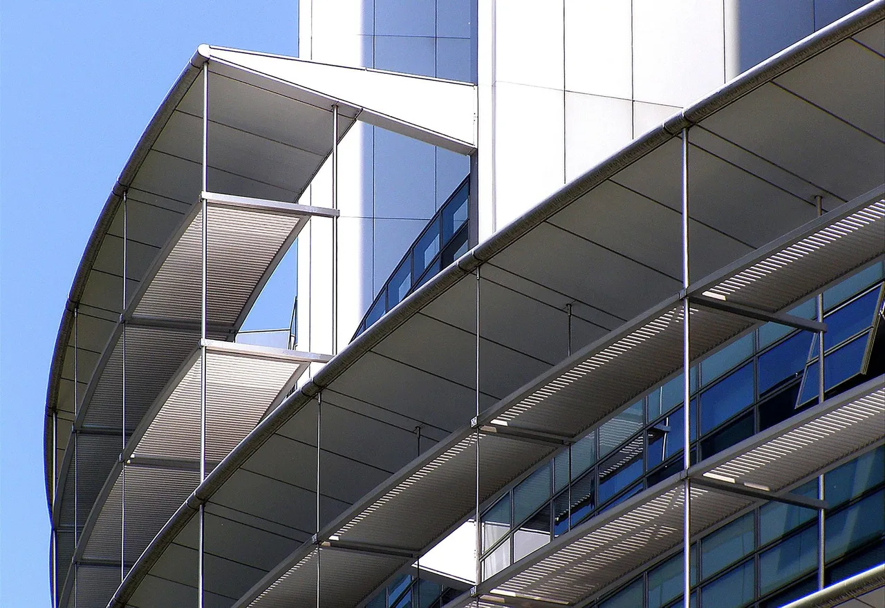 Modern office building with curved metal sunshades and blue-tinted glass windows against clear sky